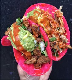 two tacos with meat, guacamole and sauce on them are held up to the camera