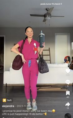 a woman in pink jumpsuits holding a bottle and purse while standing next to a couch