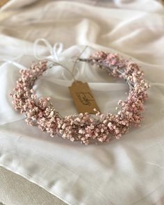 a necklace with pink flowers on it sitting on a white cloth next to a tag