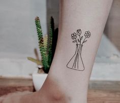 a woman's foot with a tattoo that has flowers in a vase on it