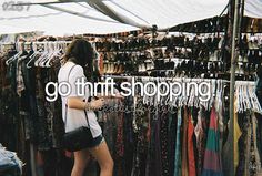 a woman standing in front of a rack of clothes and looking at her cell phone