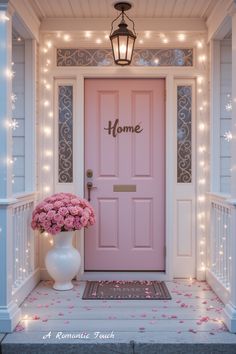 a pink front door with lights and flowers in the vase next to it is a welcome sign that says home