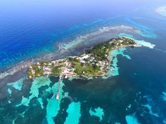 an island in the middle of the ocean surrounded by blue water and coral reefs with houses on it