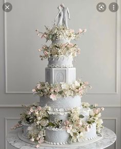 a three tiered wedding cake with flowers on the top and two figurines atop it