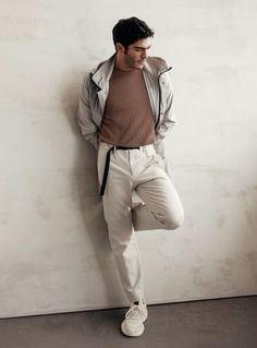 a man leaning against a wall with his hands in his pockets and wearing white pants