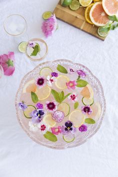 a table topped with glasses and plates filled with fruit next to sliced lemons, grapefruits and flowers