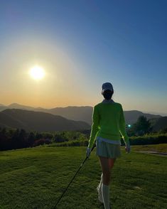 a woman is walking on the grass with her golf club in hand as the sun sets