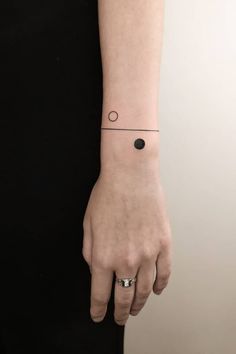 a woman's hand with a small black dot tattoo on her left wrist and an arrow