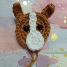 a crocheted brown and white animal head on a pink and gold painted background