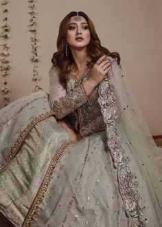 a woman sitting on top of a bed wearing a white dress with gold and silver details