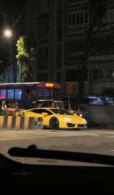 a yellow car is parked in front of a bus on the street at night time