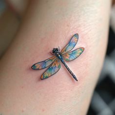 a small dragonfly tattoo on the back of a woman's thigh, it is blue and yellow