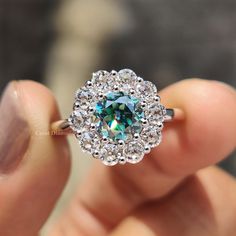 a person holding a ring with a blue diamond in it's center and surrounded by small white diamonds