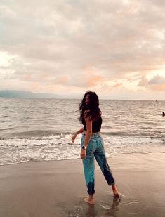 a woman standing on top of a sandy beach next to the ocean under a cloudy sky