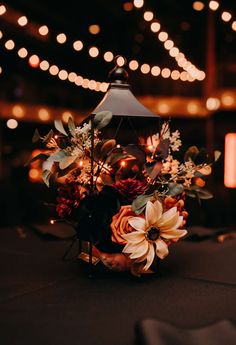 an arrangement of flowers and greenery in a vase on a table with string lights