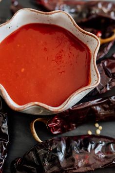 a white bowl filled with red sauce next to some chili peppers on a counter top