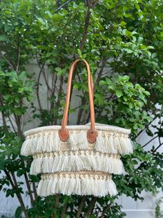 Discover the perfect blend of traditional craftsmanship and contemporary style with this stunning handmade Moroccan raffia bag. This beautiful piece features intricate woven patterns and eye-catching fringe detailing, showcasing the exceptional skill of Moroccan artisans. The bag is adorned with three tiers of elegant fringe, adding a playful yet sophisticated touch. Sturdy leather handles provide a comfortable carry, making it ideal for everyday use or special outings. Each bag is a unique creation, ensuring you have a one-of-a-kind accessory to complement any outfit. Features: *Artisan-crafted in Morocco *High-quality raffia material *Three tiers of fringe detailing *Durable leather handles *Unique, one-of-a-kind design Ideal For: *Beach trips *Shopping *Casual outings *Enhancing bohemia Natural Palm Leaf Bags With Braided Handles, Chic Handwoven Natural Fiber Bucket Bag, Woven Natural Fiber Bucket Bag For Shopping, Cream Woven Tote Shoulder Bag, White Bohemian Bucket Beach Bag, Bohemian White Bucket Beach Bag, White Bohemian Rectangular Bucket Bag, Bohemian White Bag For Vacation, White Fringe Travel Bag