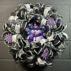 a wreath with a snowman on it hanging against a brick wall in front of a black and white door