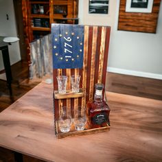 an american flag made out of wooden crates with whiskey glasses on the table in front of it