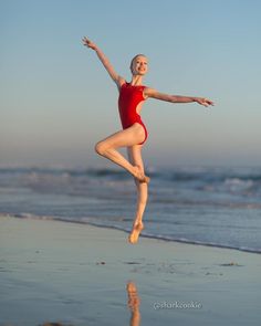 a woman in a red leotard jumping on the beach