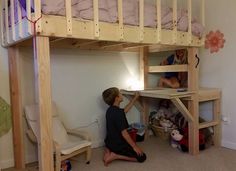 a young boy sitting on the floor under a bunk bed next to a desk and chair