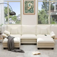 a living room with a white couch and book on the floor in front of large windows