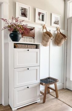 a white cabinet with two baskets on top of it next to a stool and pictures