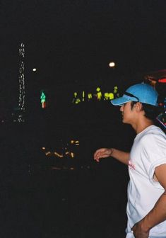 a man in white shirt and blue hat standing next to a building at night with lights on