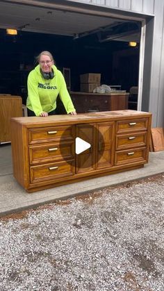 a man standing next to a wooden dresser in front of a garage door with his hands on the drawers