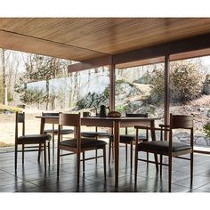 a dining room table with four chairs and a vase on the table in front of large windows