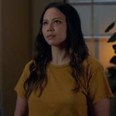 a woman standing in front of a window wearing a yellow shirt and looking off to the side