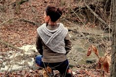 a woman sitting on the ground in front of some trees and leaves with her back turned to the camera