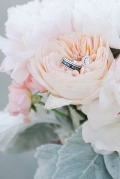 two wedding rings sitting on top of a bouquet of white and pink flowers with leaves