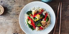 a white plate topped with chicken and veggies next to chopsticks on top of a wooden table