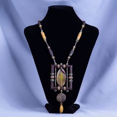 This handcrafted piece from Central Asia is a celebration of natural beauty and artisan skill. The pendant showcases a magnificent agate stone, known for its fine grains and warm, translucent hues. This agate has been masterfully cut into an eye-catching teardrop shape, exhibiting a mottled pattern with swirls of yellow, amber, and fiery orange, resembling a sunset captured in stone. The agate is framed by a square border crafted from natural leather, dyed a deep, rich brown that contrasts the s Brown Agate Necklace, Brown Agate Pendant Necklaces, Brown Multi-strand Necklaces With Natural Stones, Square Border, Unique Brown Multi-strand Necklace, Brown Agate Hand-strung Necklaces, Leather Frames, Handcrafted Necklace, Leather Gifts