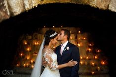 a bride and groom kissing in front of candles