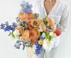 a woman holding a bouquet of flowers in her hands and wearing a white shirt with long sleeves