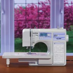 a white sewing machine sitting on top of a wooden table next to a pink tree