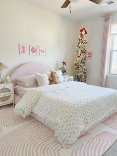 a bedroom decorated in pink and white with a christmas tree on the wall behind the bed