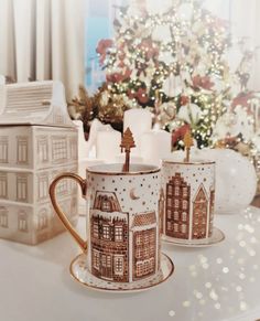 two coffee mugs sitting next to each other on a table near a christmas tree