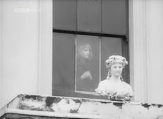 an old black and white photo of a woman looking out the window