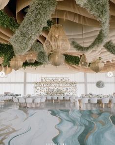 a room with tables and chairs covered in greenery, hanging lights and chandeliers