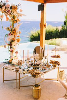 a table with flowers and candles on it next to the ocean in front of a gazebo