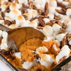 a spoon is scooping some food out of a casserole dish with marshmallows and pecans