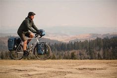 a man riding a bike on top of a dirt road next to trees and mountains