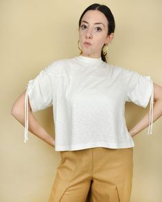 a woman standing with her hands on her hips wearing brown pants and a white top