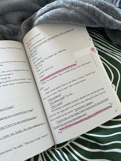 an open book sitting on top of a bed next to a gray and white blanket