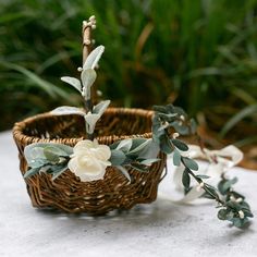 a flower arrangement in a basket on a table next to greenery and flowers,