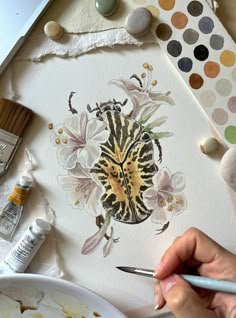 a person is painting flowers on a piece of paper with watercolors and paintbrushes