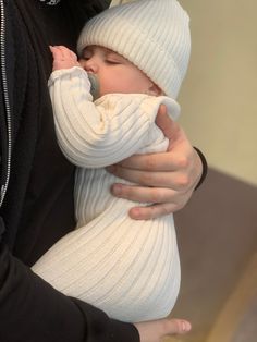 a man holding a baby in his arms while wearing a white knitted hat and sweater